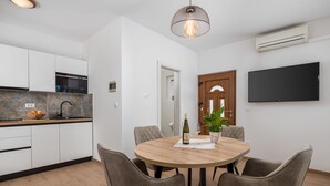 Cocina moderna con armarios blancos, un microondas y un lavabo. Hay una mesa de comedor con sillas y una planta en maceta.