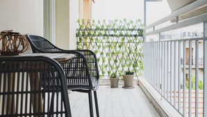 Ein Balkon mit zwei schwarzen Stühlen, einem kleinen Tisch und zwei Blumentöpfen.