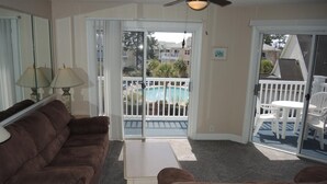 A living room with a brown couch, a small table, and a sliding glass door leading to a balcony with a pool.
