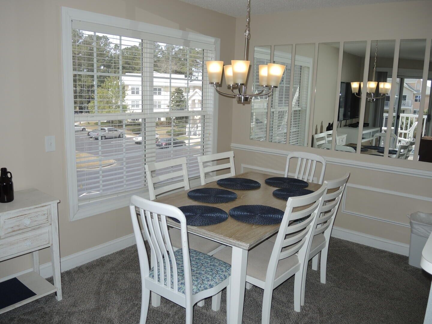 A dining room with a wooden table, white chairs, and a chandelier.