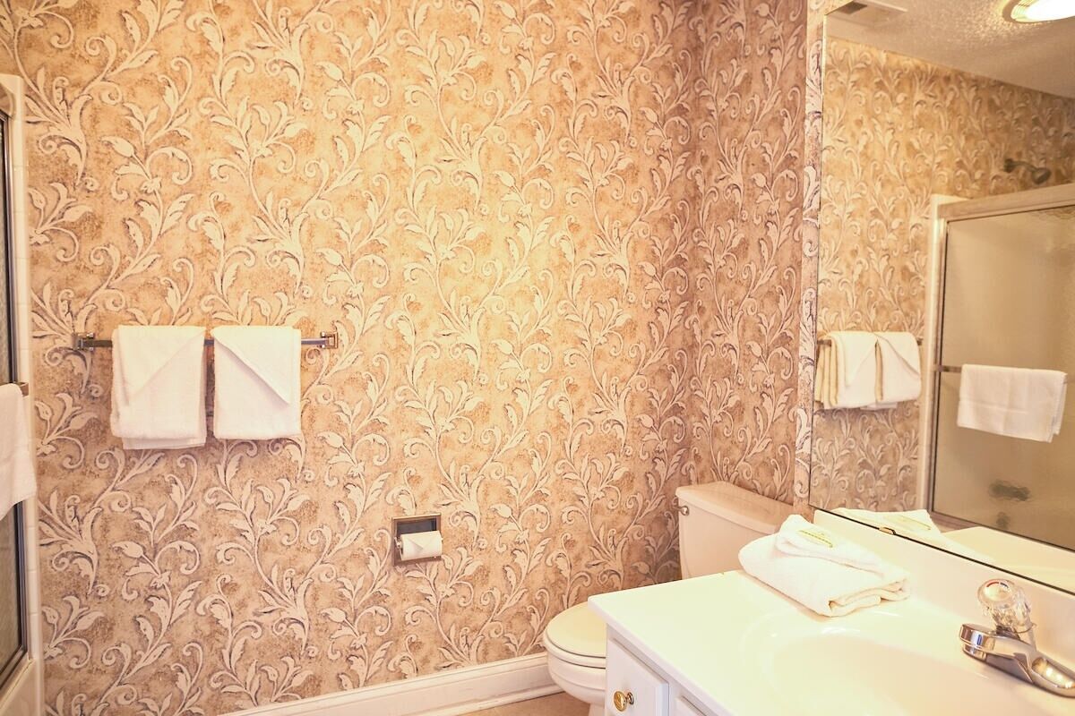 A bathroom with a patterned wallpaper, a white sink, a mirror, and a toilet.