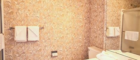 A bathroom with a patterned wallpaper, a white sink, a mirror, and a toilet.