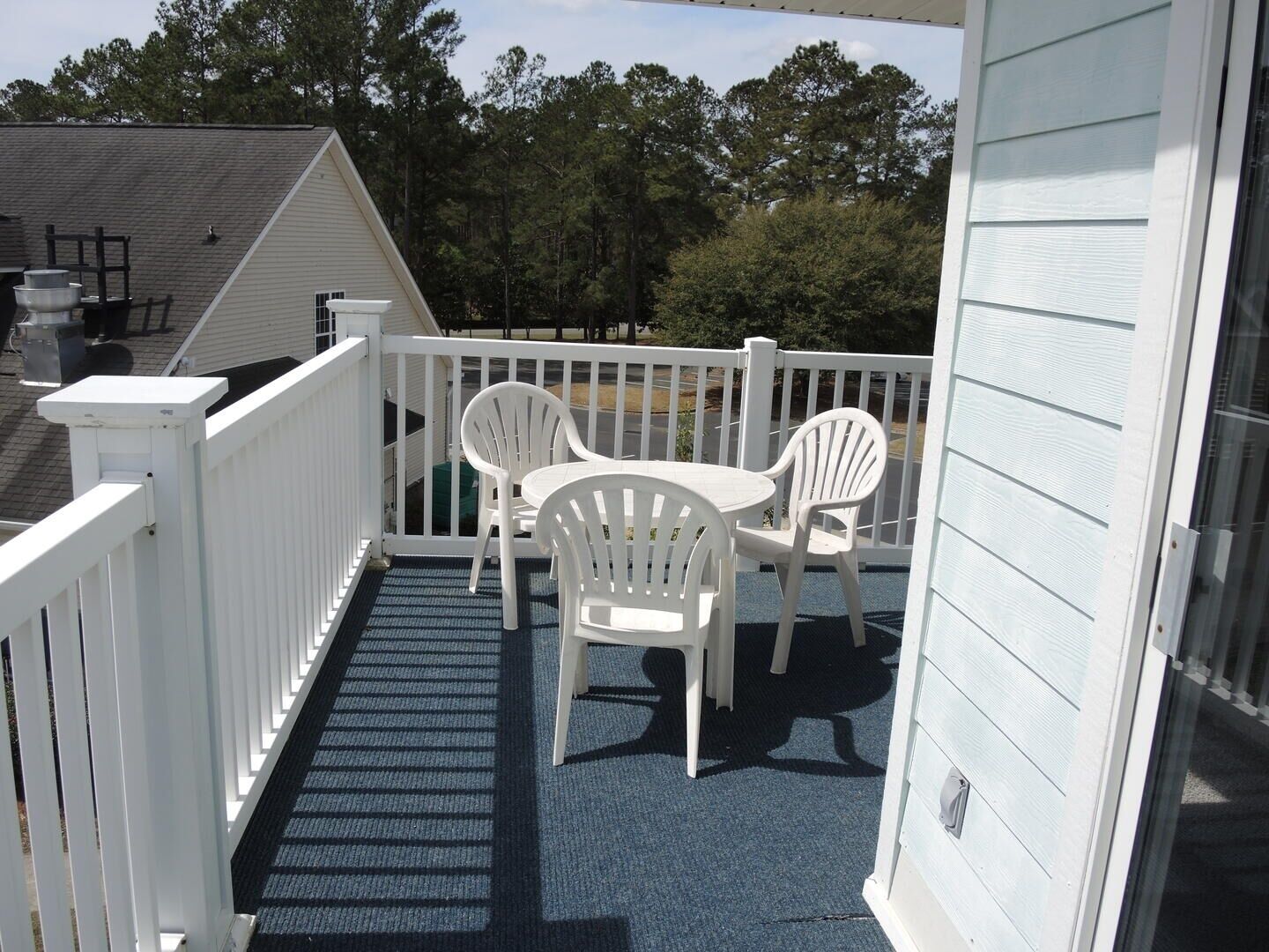 A balcony with a blue carpet, white railing, and two white plastic chairs.