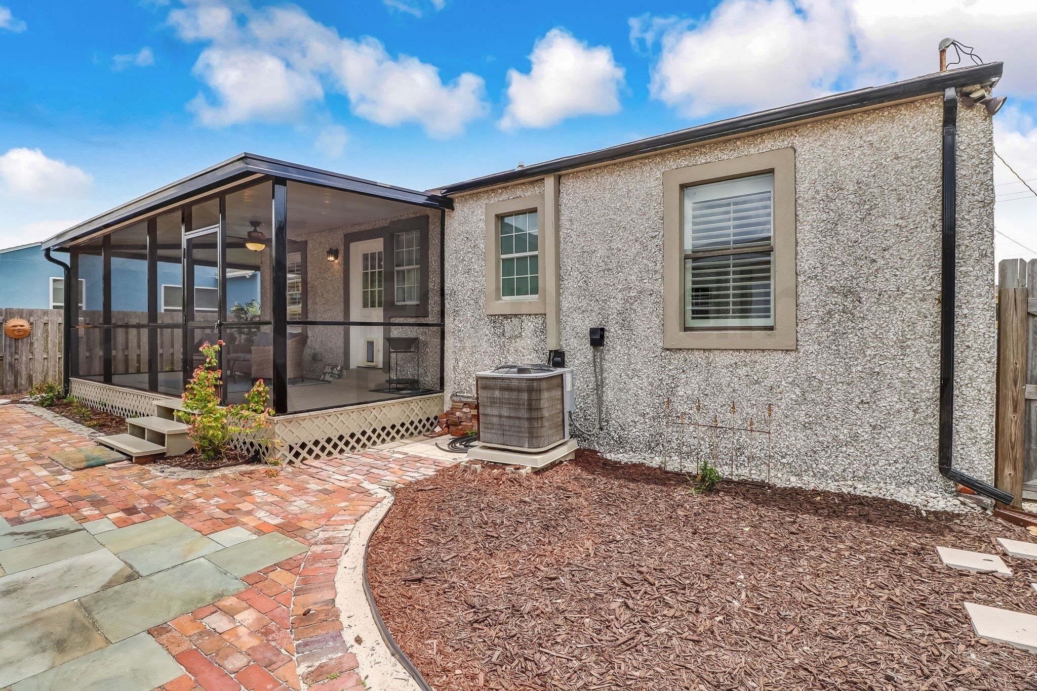 A residential house with a covered patio, a stone exterior, and a small garden area with mulch.