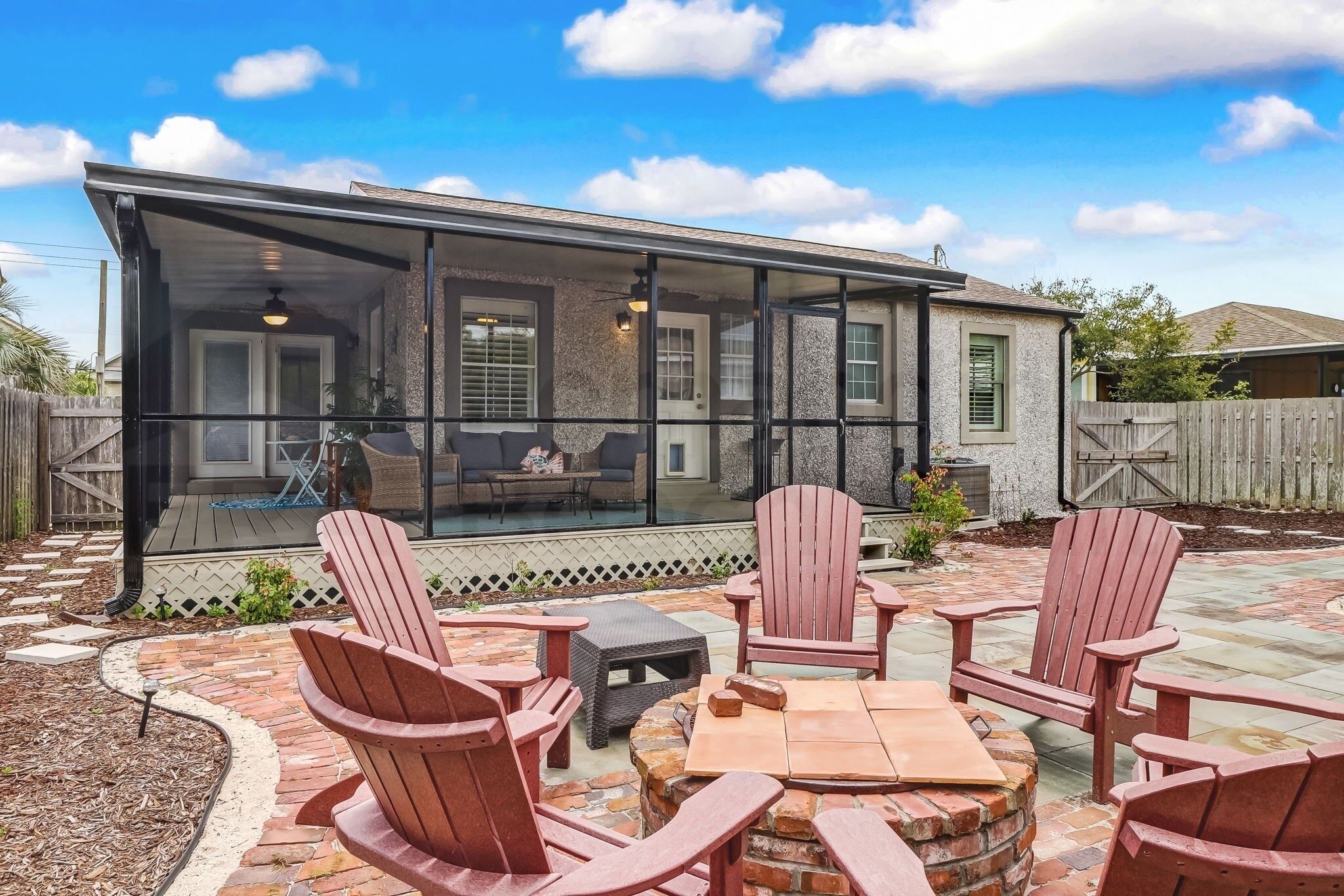 A covered patio with Adirondack chairs and a fire pit, overlooking a backyard.