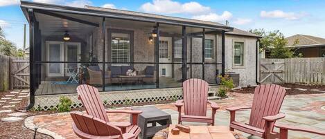 A covered patio with Adirondack chairs and a fire pit, overlooking a backyard.