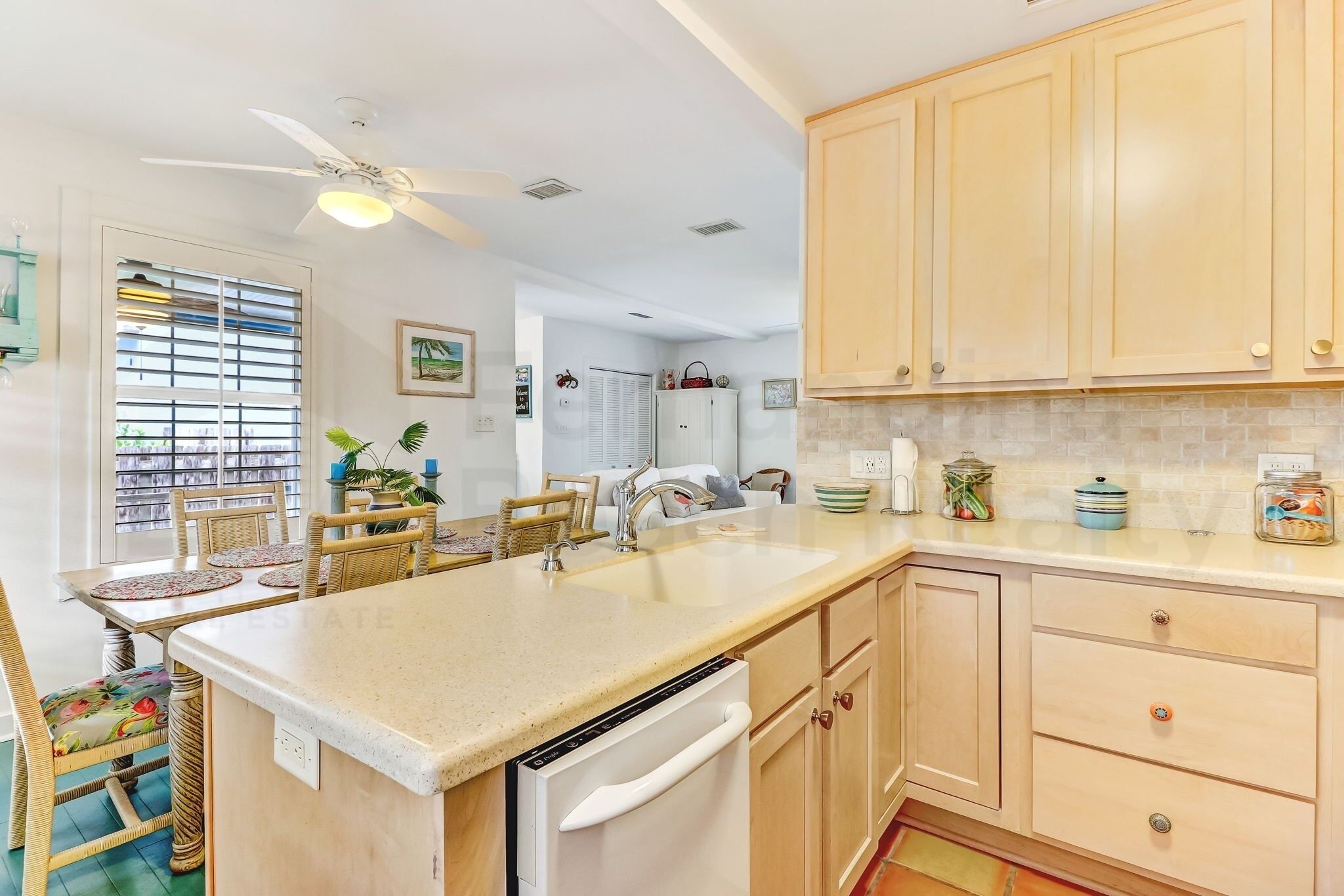 A kitchen with wooden cabinets, a white dishwasher, and a dining area with wicker chairs and a table.