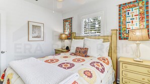 A bedroom with a bed, a nightstand, a dresser, a window with blinds, and a ceiling fan.