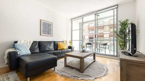 A modern living room with a black leather sofa, a wooden coffee table, and a large sliding glass door leading to an outdoor balcony. - A Modern & Stylish Studio Next to Darling Harbour (Sydney)