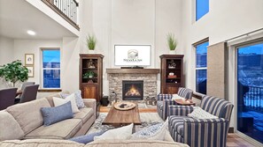 Een ruime woonkamer met een open haard, comfortabele zithoek en een groot raam met uitzicht.