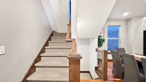 Un escalier avec des rampes en bois mène à une salle à manger qui offre une vue sur l’extérieur.