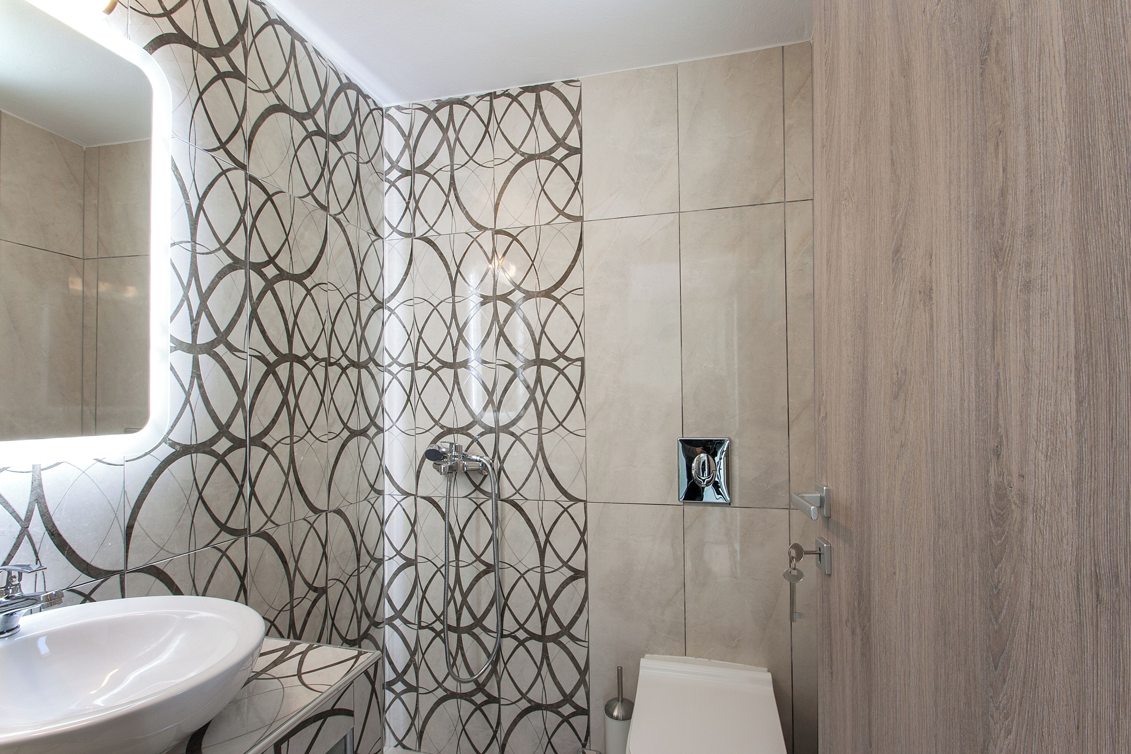 A bathroom with a patterned tile wall, a sink, and a toilet.