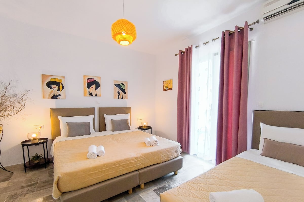 A hotel room with a large bed, a smaller bed, two bedside tables with lamps, and artwork on the walls.