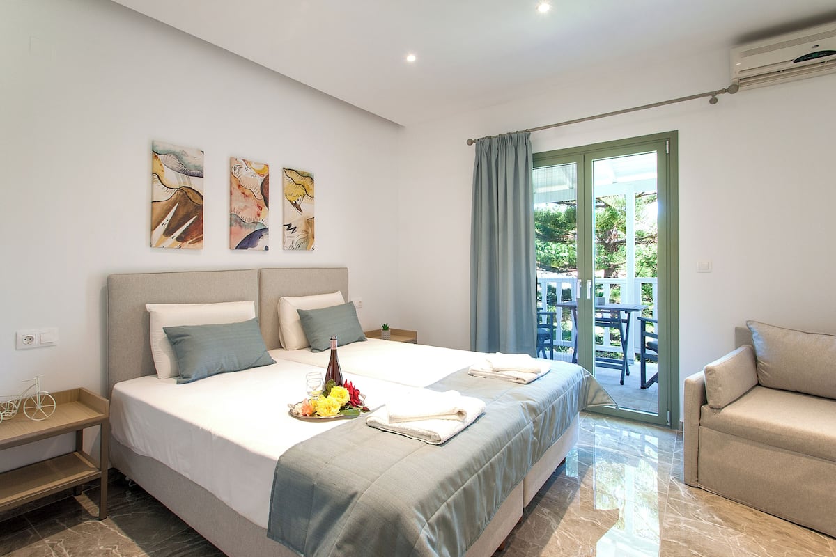 A hotel room with a large bed, a sofa, and a balcony with a table and chairs.
