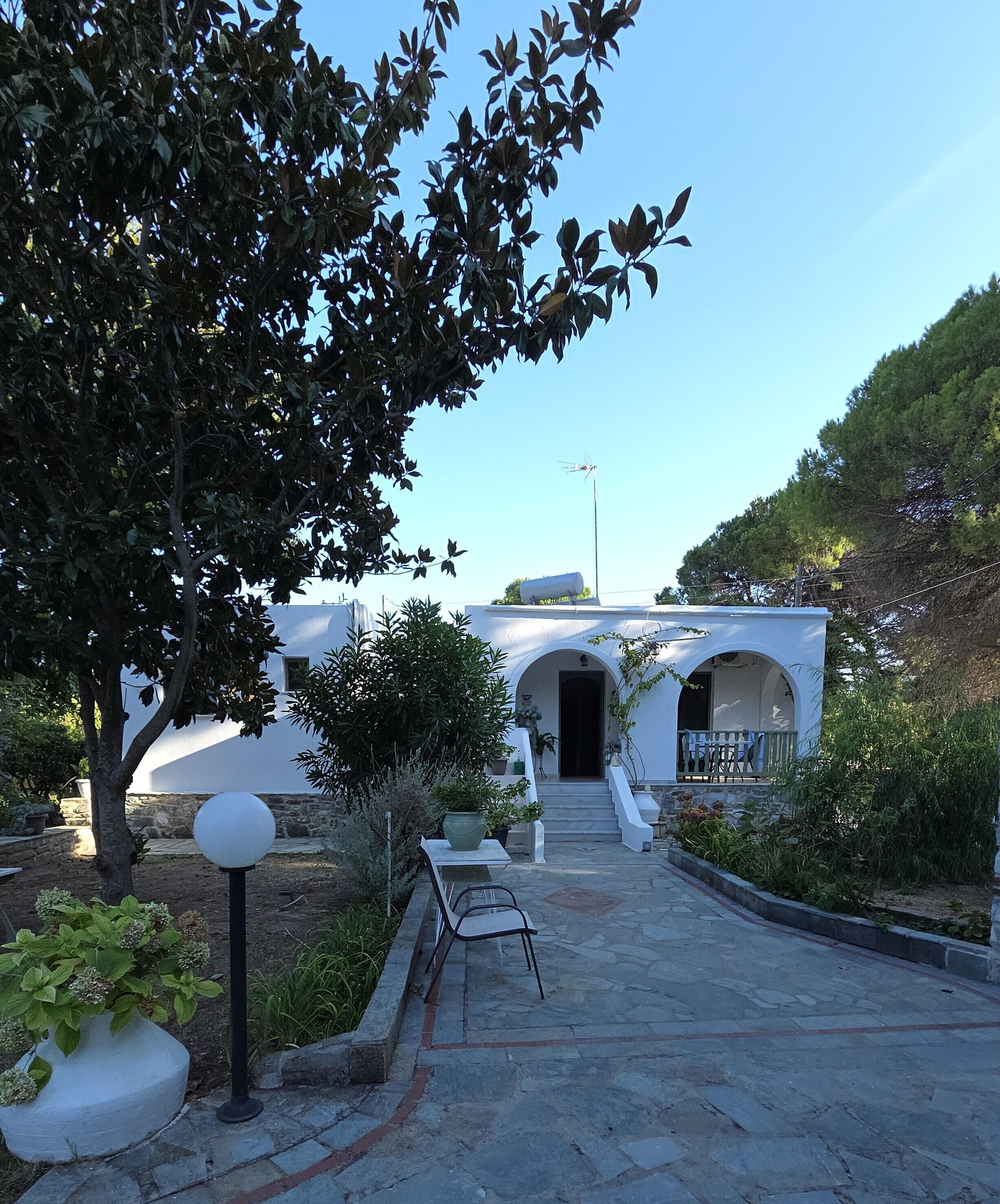 A pathway leading to a building with a white facade and arched entrance. There is a bench and a potted plant along the path.