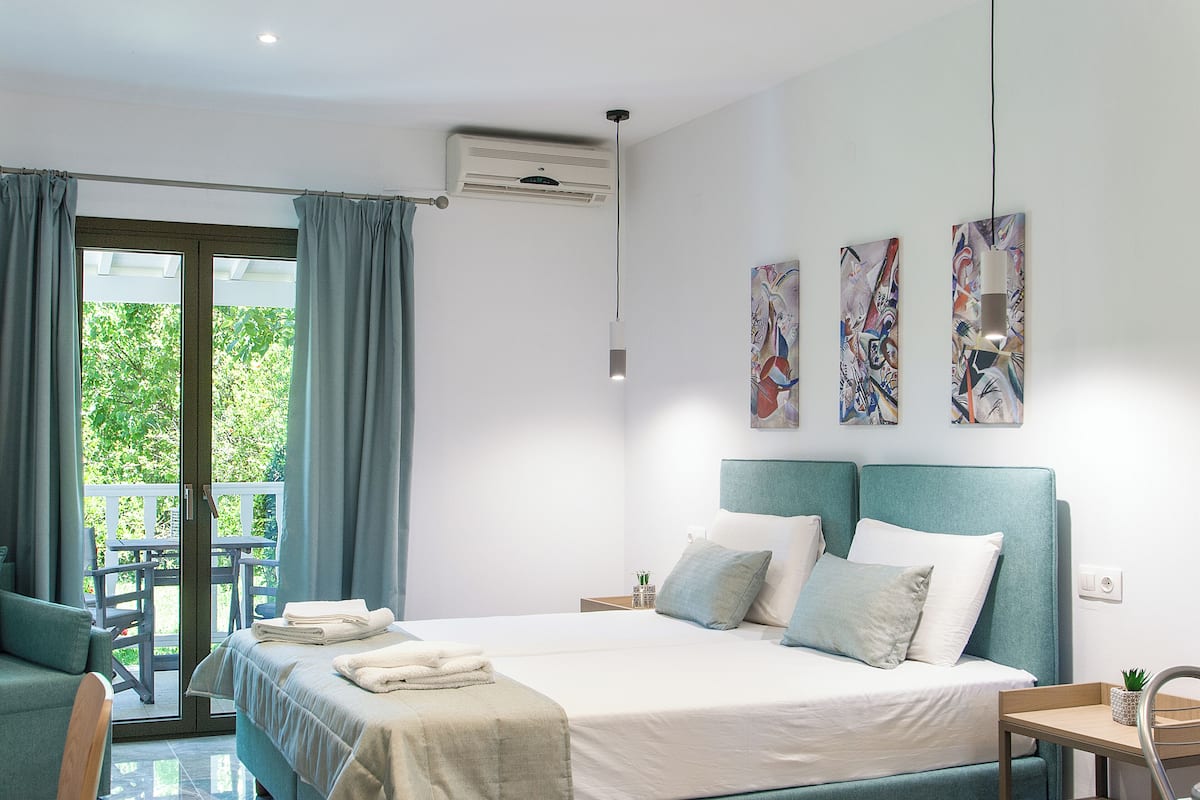 A modern hotel room with a large bed, a desk, and a balcony with a table and chairs.