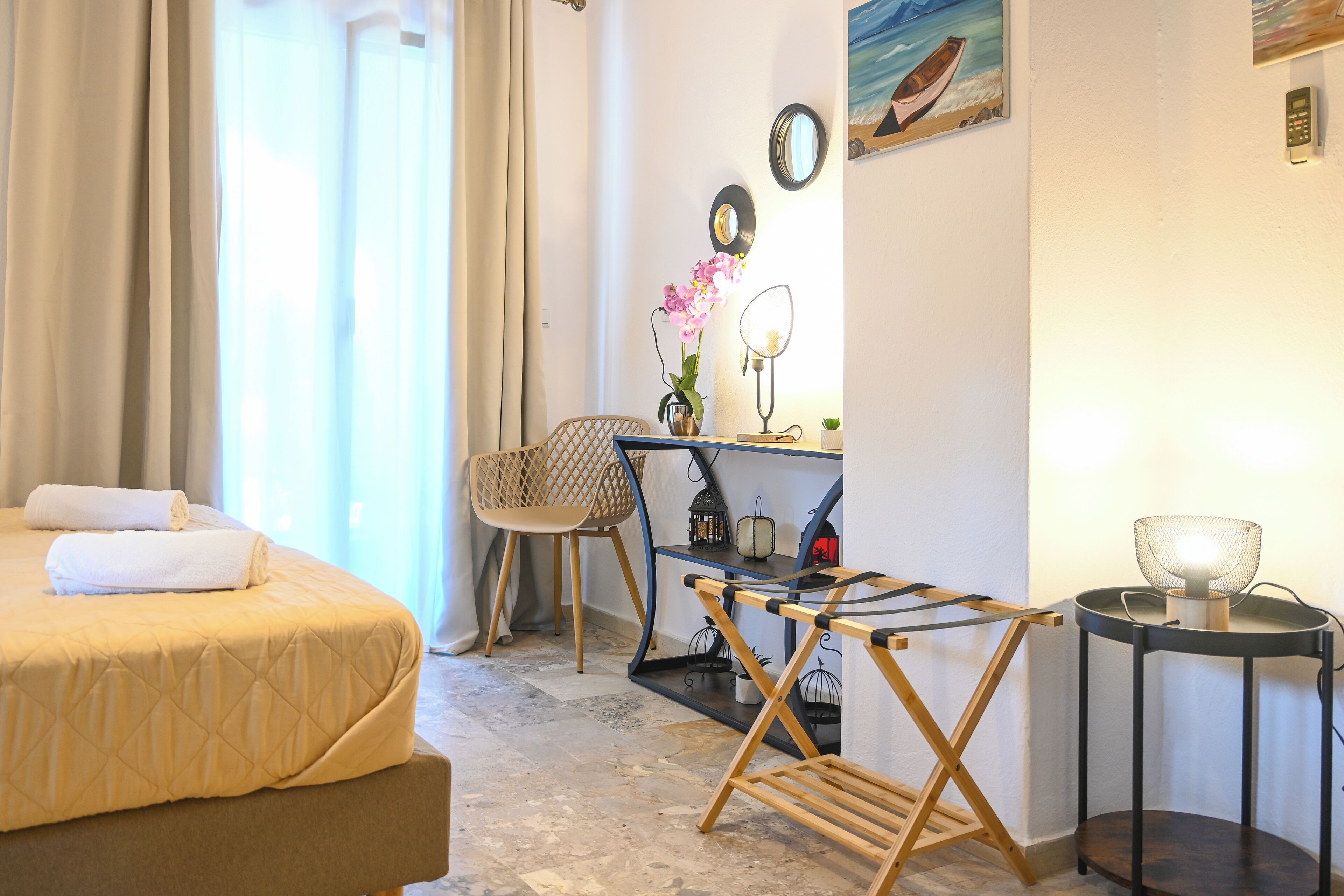 A hotel room with a bed, a desk with a lamp, a chair, and a small table with a lamp.