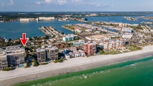 Vue aérienne d’une ville côtière, avec un hôtel en bord de mer, un port de plaisance et des immeubles résidentiels environnants.
