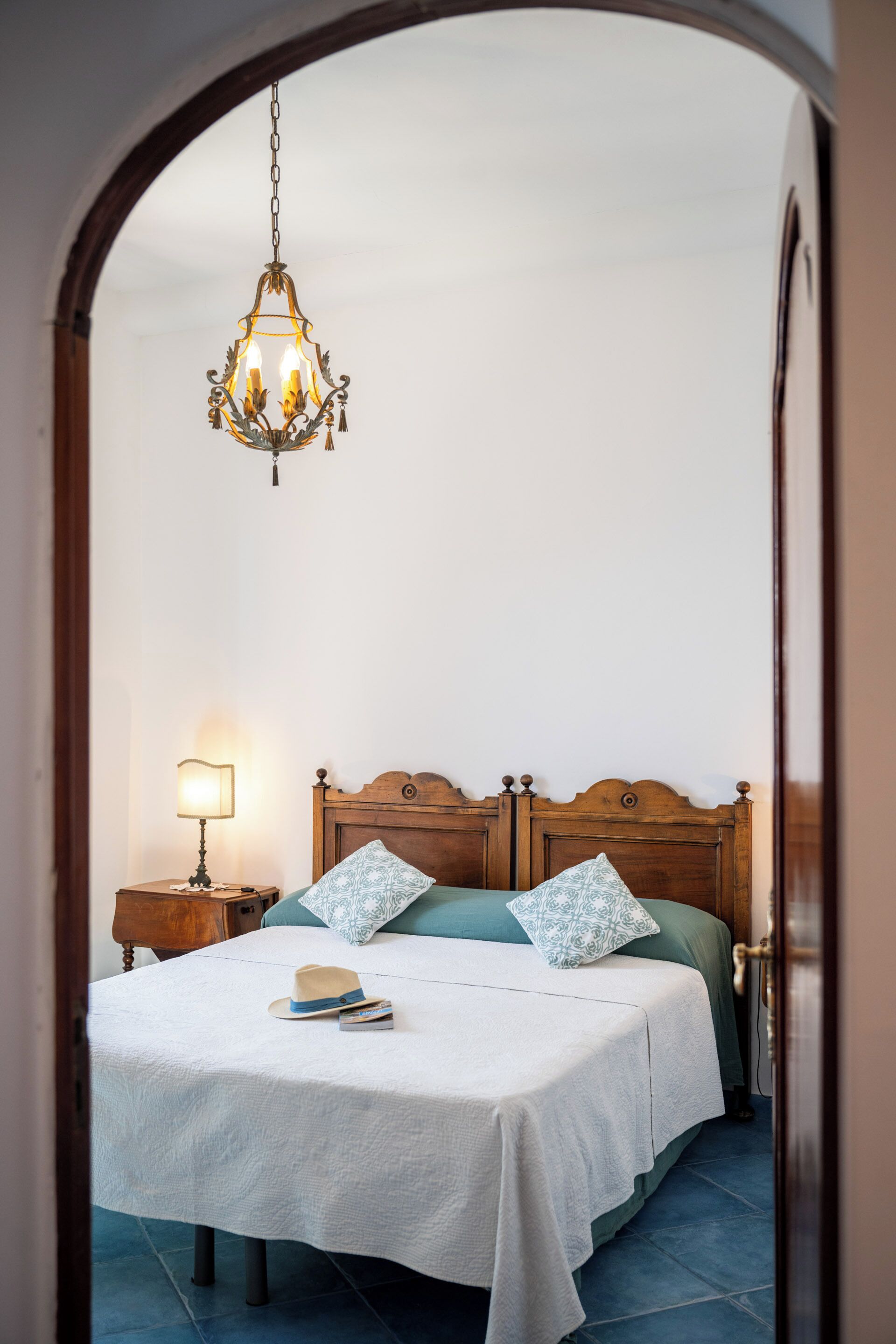 A bedroom with a wooden headboard, a white bedspread, two pillows, a bedside lamp, and a hanging light fixture.