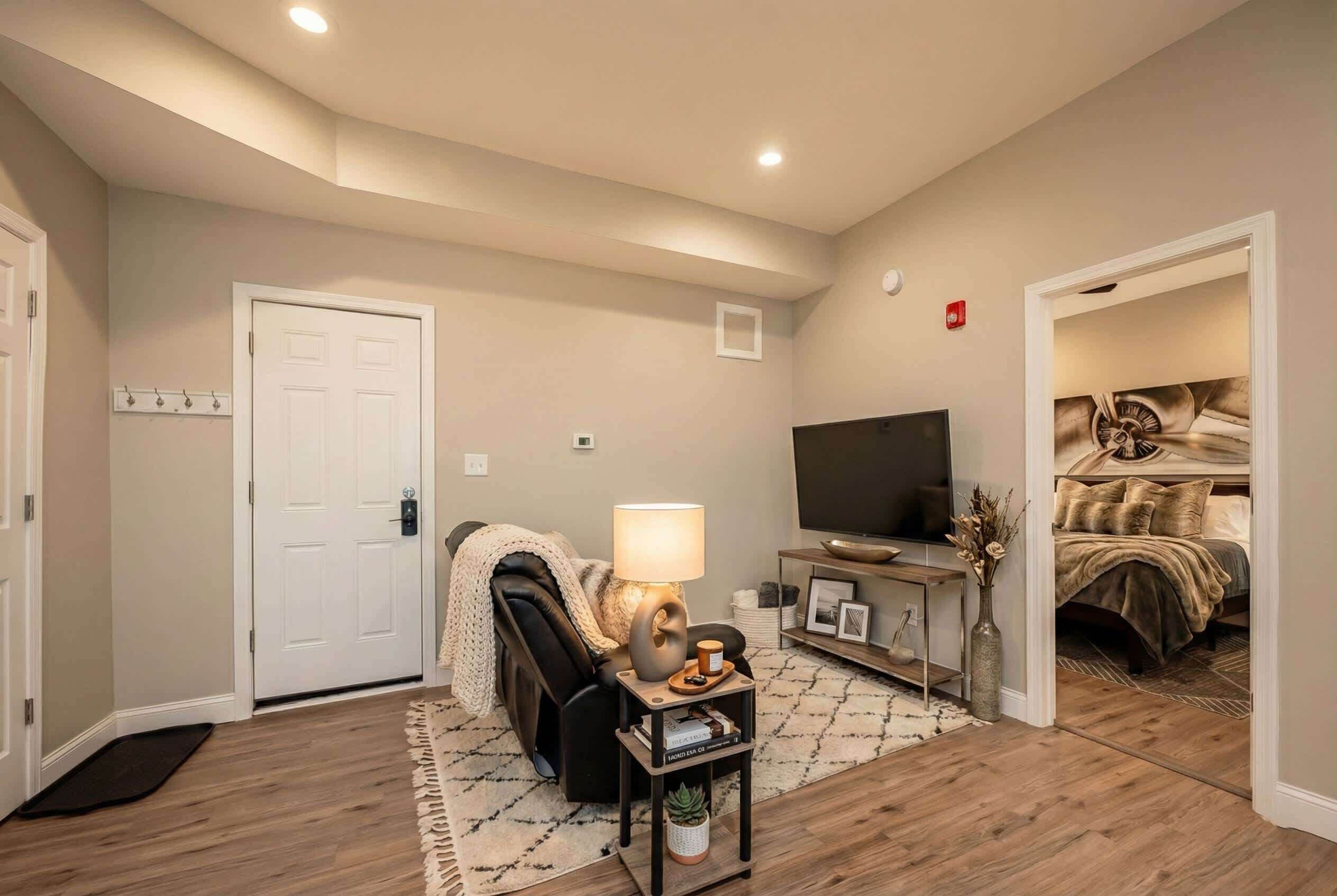 Un salon comprenant un canapé, une table basse, un téléviseur et une porte donnant sur une chambre.