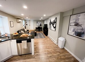 A modern kitchen with a central island, a dining area with a sofa, and a living room with a TV. - Stylish Cool Springs Apt, King Bed (Wilmington)