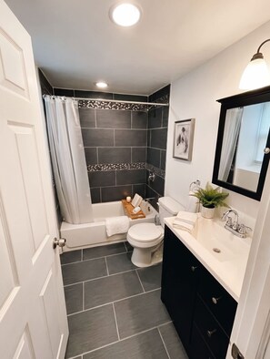 A modern bathroom with a bathtub, toilet, and sink. - Stylish Cool Springs Apt, King Bed (Wilmington)