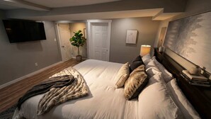 A bedroom with a large bed, a flat-screen TV, a potted plant, and a painting on the wall. - Stylish Cool Springs Apt, King Bed (Wilmington)