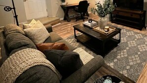 A living room with a sofa, coffee table, TV, and a desk with a chair. - Stylish Cool Springs Apt, King Bed (Wilmington)