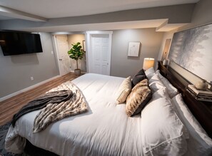 A bedroom with a bed, a TV mounted on the wall, a door, a plant, and a painting. - Stylish Cool Springs Apt, King Bed (Wilmington)