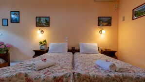 A hotel room with two beds, floral bedding, wall-mounted lamps, a nightstand with a vase of flowers, and framed pictures on the walls. - Villa Sophia by CorfuEscapes (Corfu)