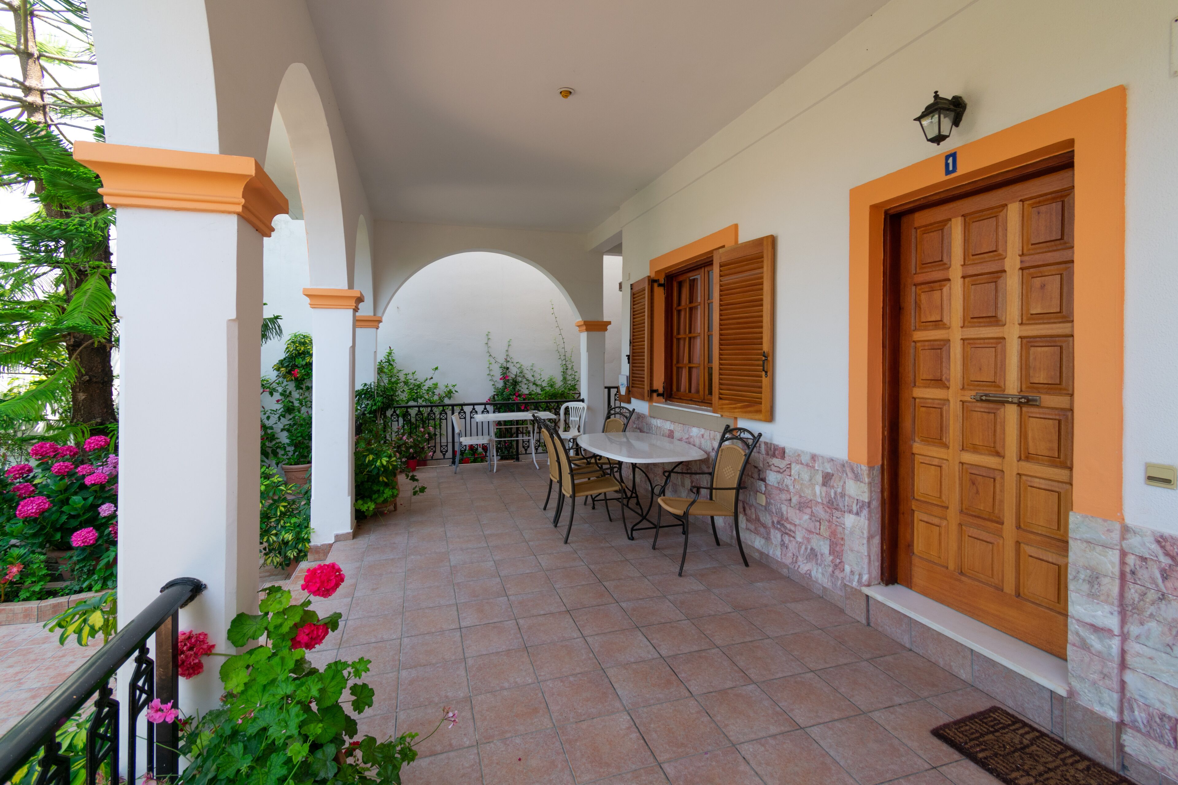 Un porche cubierto con una mesa, sillas, una puerta de madera y macetas con plantas.