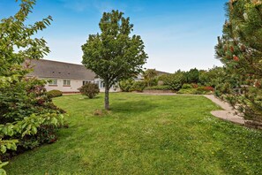 A residential area with a well-maintained lawn, a single tree, and a house with a sloped roof.