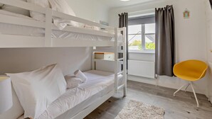 Quarto com beliche, janela, uma cadeira amarela e abajur branco.