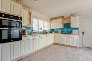 A kitchen with white cabinets, a black oven, a coffee maker, and a toaster. - 3 Bed in Woolacombe (oc-dreams) (Woolacombe)