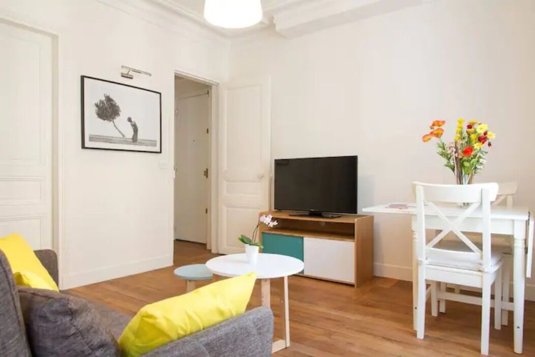 A living room with a sofa, a small round table, a TV on a wooden stand, and a white chair.