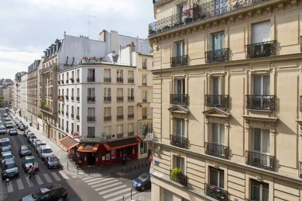 Vista de una calle con hileras de edificios europeos clásicos con balcones, un paso de cebra y coches aparcados.