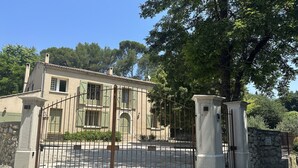 A two-story building with a traditional architectural style, featuring a stone facade, green shutters, and a gated entrance. - Old mill in the Luberon (Mérindol)