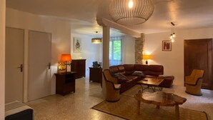 A living room with a sofa, coffee table, and lamps. There is a door, a painting, and a window. - Old mill in the Luberon (Mérindol)