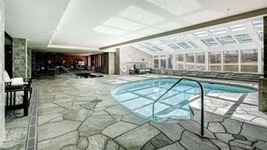 Une piscine intérieure dotée d’un sol en pierre, d’une rambarde en verre et offrant une vue sur l’extérieur grâce à de grandes fenêtres.