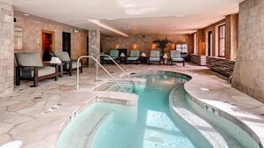 Un espace piscine doté de chaises longues, d’un jacuzzi et de murs en pierre.
