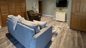 A living room with a grey sofa, wooden flooring, a television, and a wooden door.