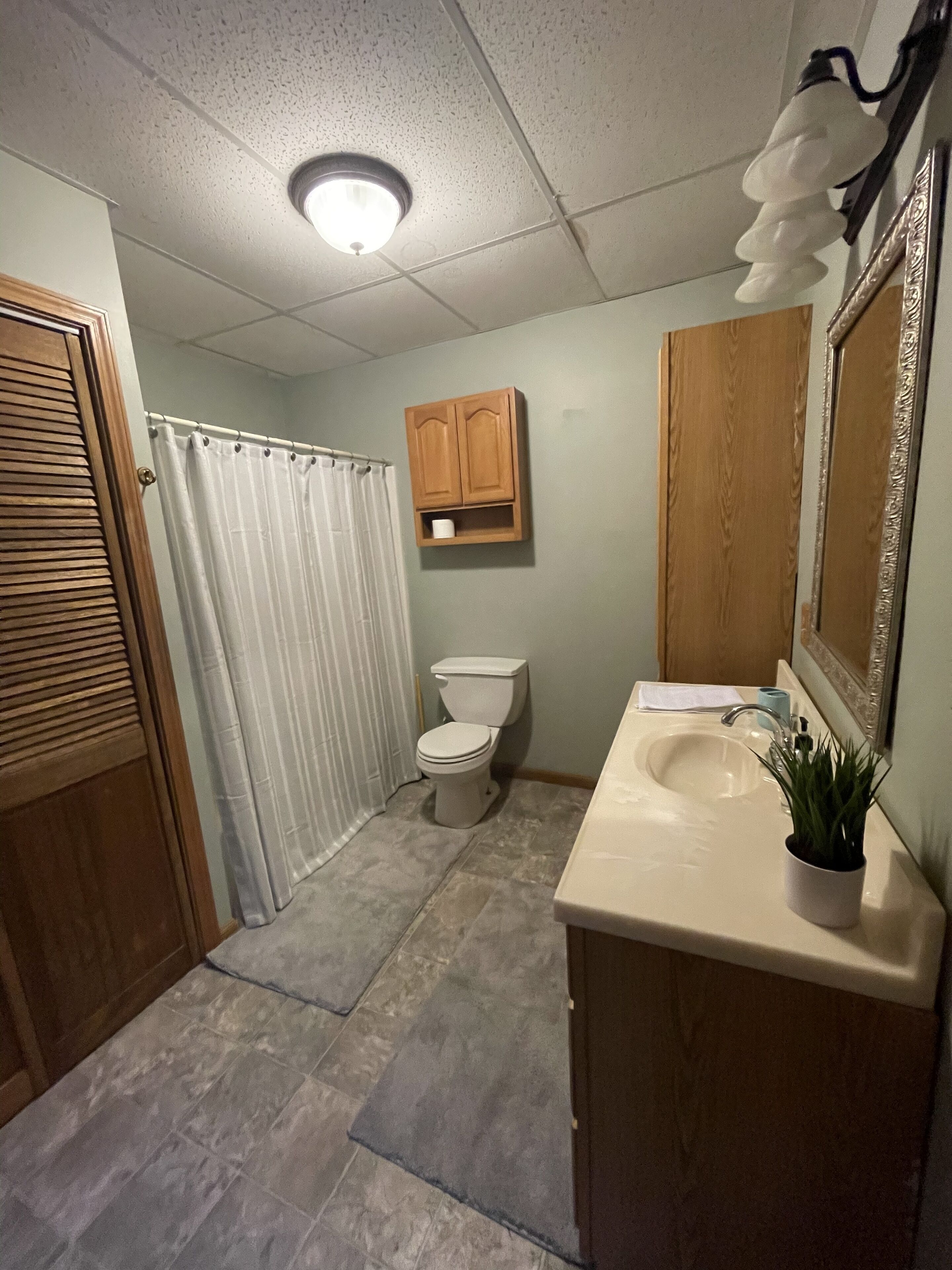 A bathroom with a toilet, a sink, a shower curtain, and a cabinet.
