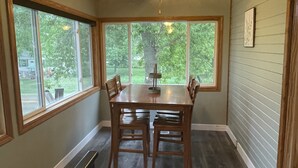 A dining area with a wooden table and chairs, large windows, and a ceiling fan.