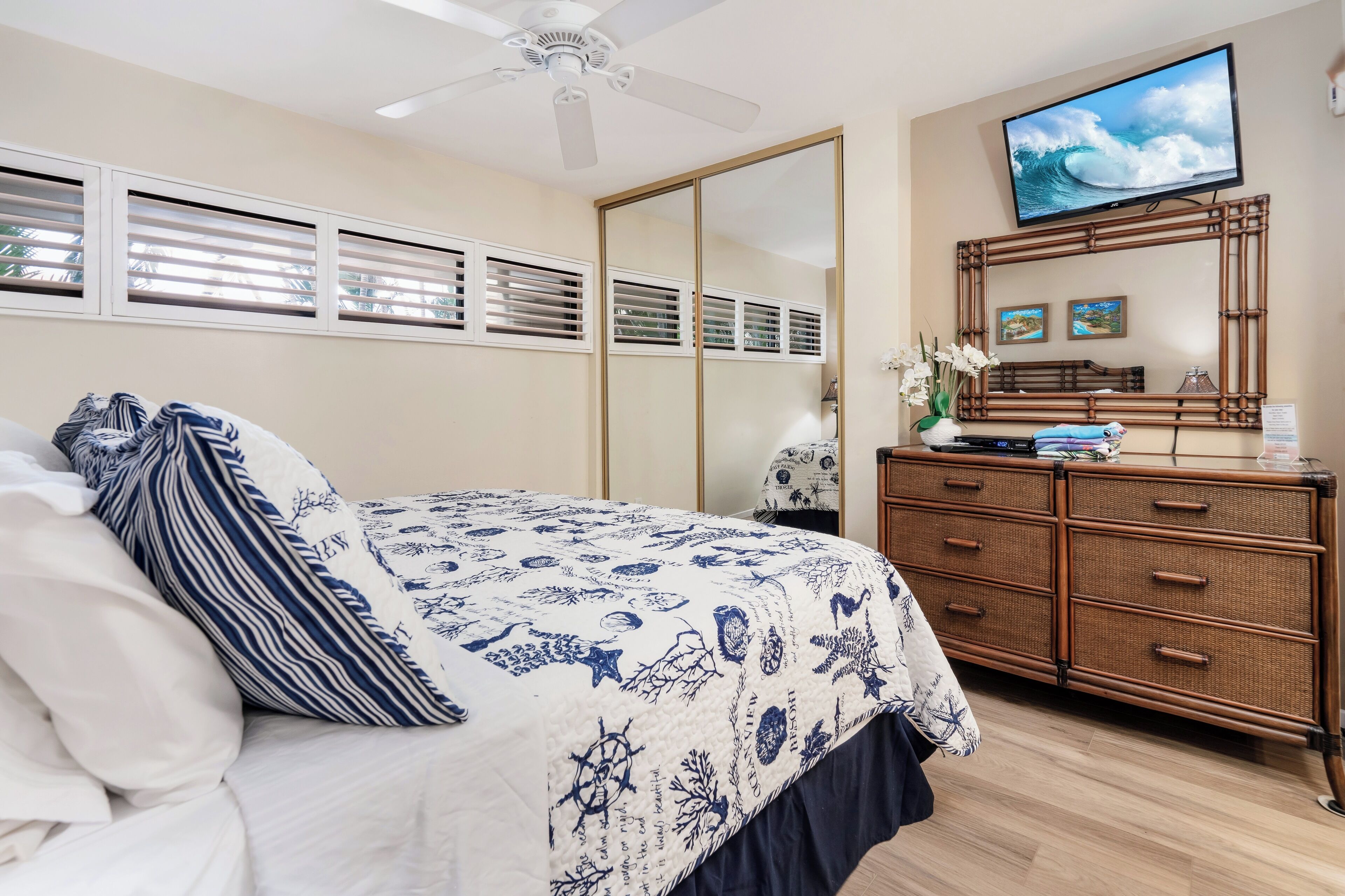 A bedroom with a bed, a ceiling fan, a television, a dresser, and a mirror.