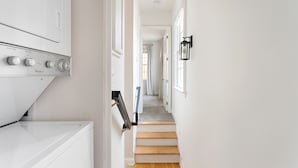 Ett tvättrum med en tvättmaskin och en torktumlare som man fyller från framsidan, en trätrappa och en hall som leder till ett annat rum.