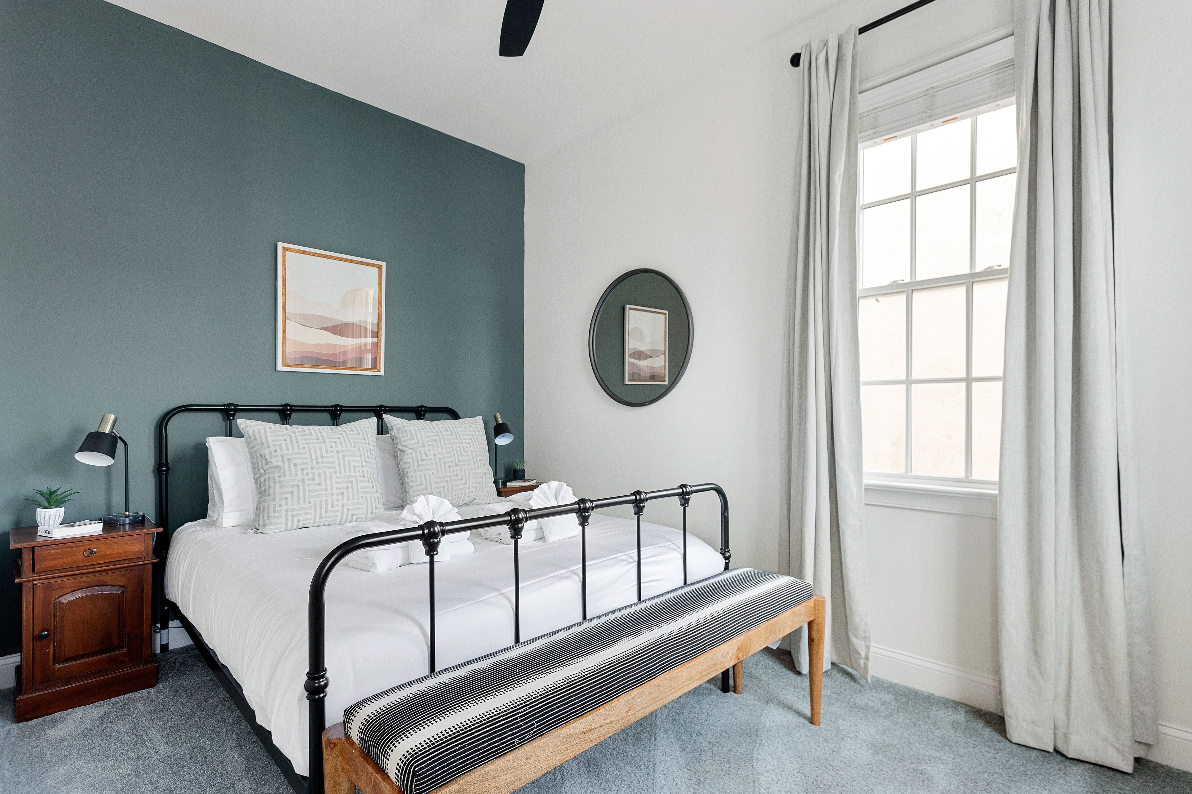 Un dormitorio con cama, mesita de noche, lámpara y ventana con cortinas.
