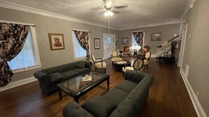 A spacious living room with a dark green sofa, a glass coffee table, and a ceiling fan. - Lg Historic.  2 bulk MSU. Hammond.  OTC.  Downtown close (Springfield)