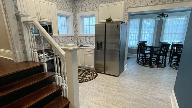 A kitchen with white cabinets, a stainless steel refrigerator, and a dining area with a table and chairs. - Lg Historic.  2 bulk MSU. Hammond.  OTC.  Downtown close (Springfield)