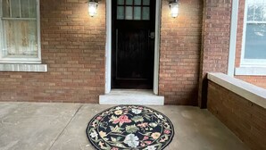 A brick entrance with a black door, two wall-mounted lights, and a floral rug on the concrete floor. - Lg Historic.  2 bulk MSU. Hammond.  OTC.  Downtown close (Springfield)