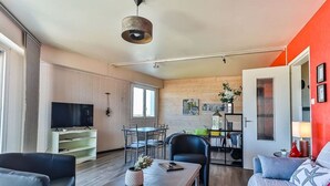 Ein modernes Wohnzimmer mit Flachbildfernseher, einem Essbereich mit Tisch und Stühlen und einer Küche im Hintergrund.